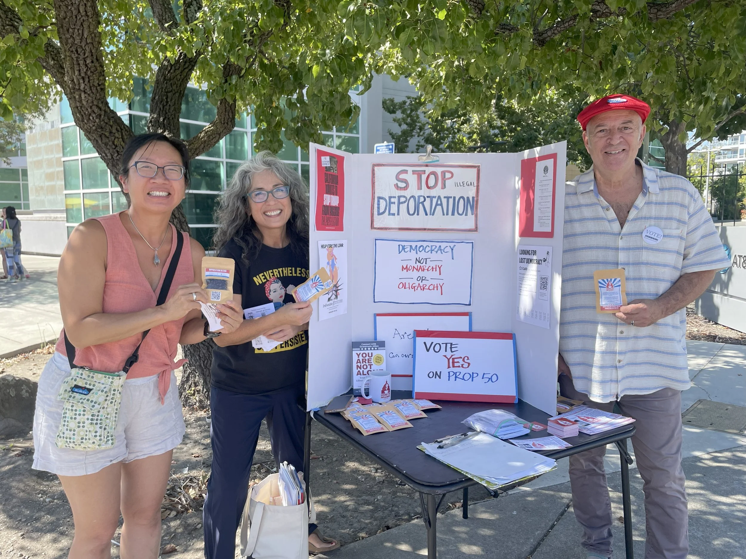 RAEB volunteers tabling with Stop Illegal Deportation and Vote Yes on Prop 50 signs